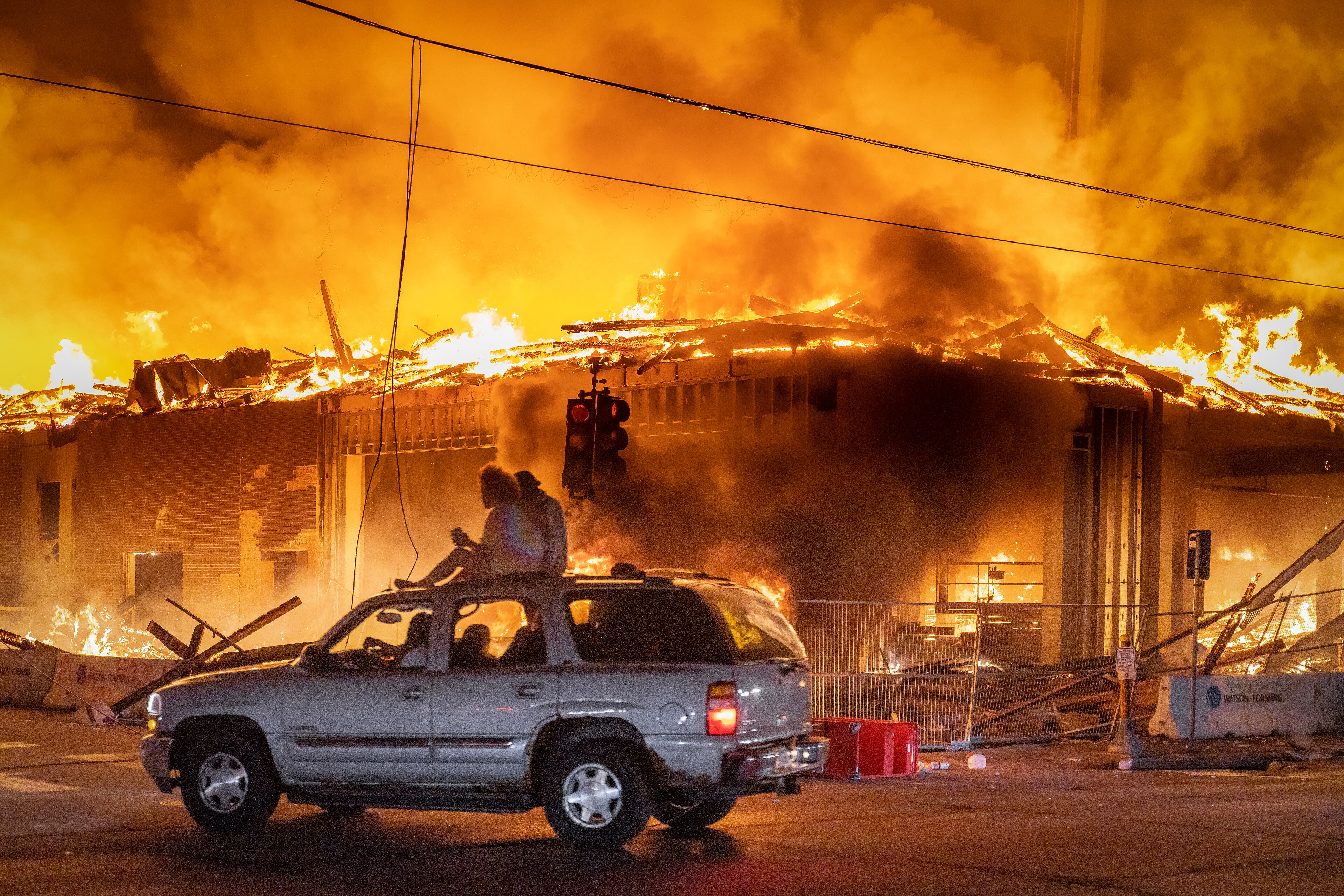 People ride atop a vehicle beside a burning Minneapolis building. Unrest followed George Floyd’s death in police custody and protests against police violence and racism.