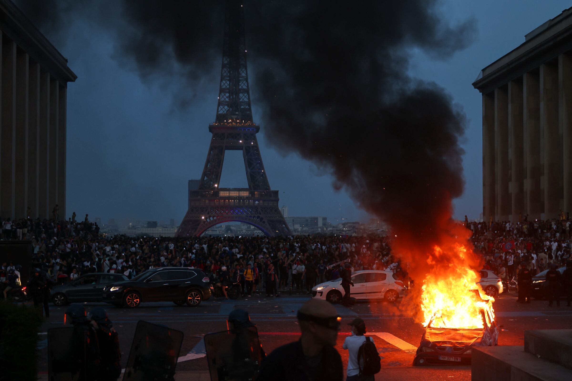 A car burns among crowds facing the Eiffel Tower. Celebrations of PSG’s Champions League victory spilled into unrest, fires and confrontations with police in Paris.
